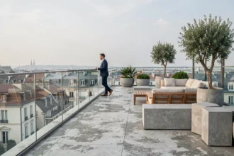 Terrasse panoramique d'un penthouse moderne avec vue sur les toits d'une ville européenne, homme en blazer marine contemplant le paysage urbain